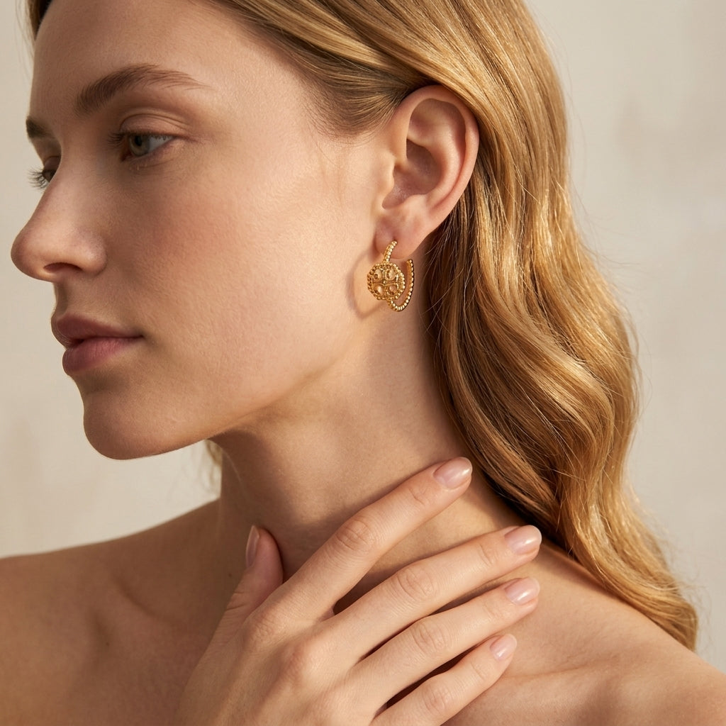 A close-up side profile of a woman with blonde hair wearing a delicate gold hoop earring with a textured, floral-like pattern.