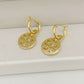 Gold hoop earrings with circular disc charms on a white surface