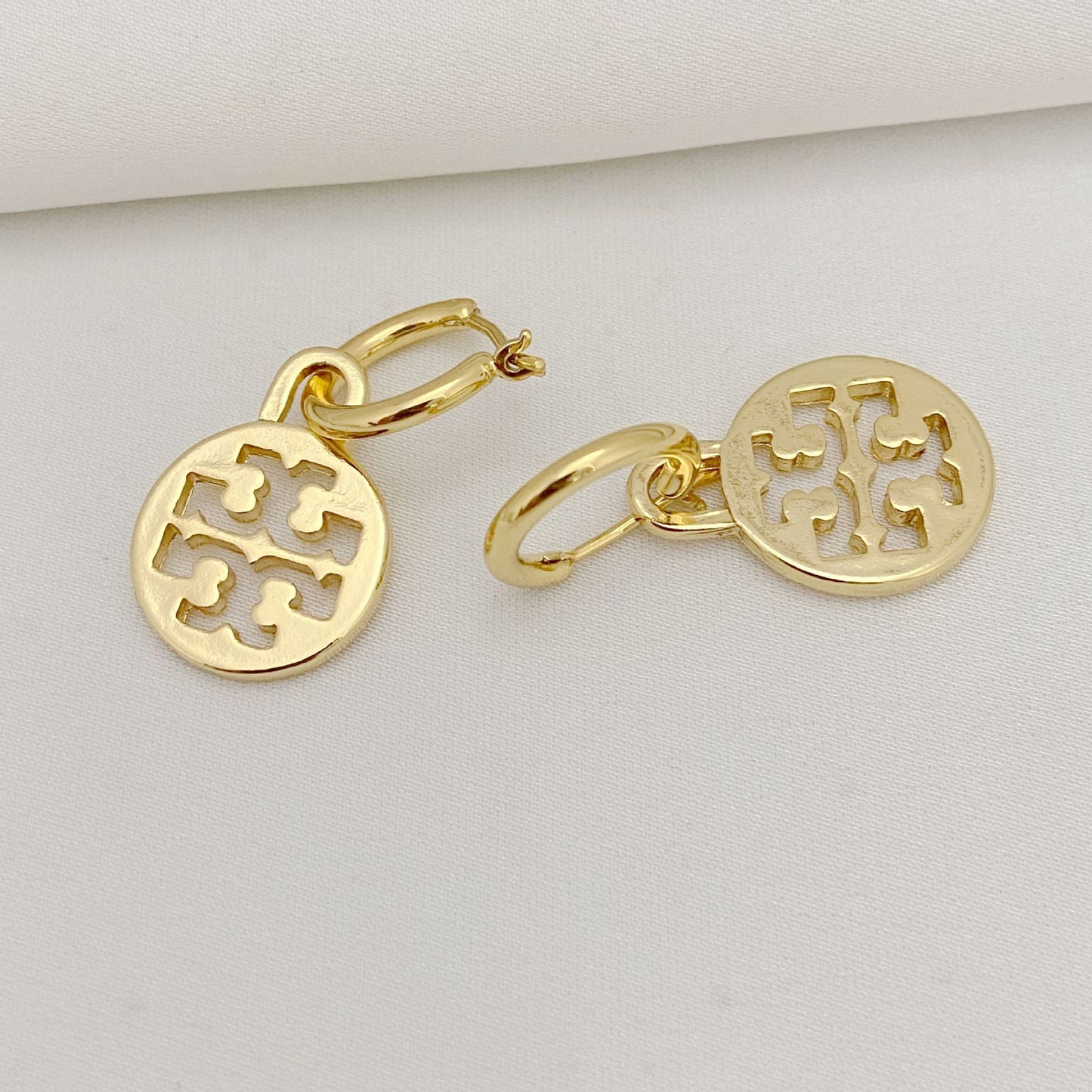 Gold hoop earrings with circular designs on a light gray background