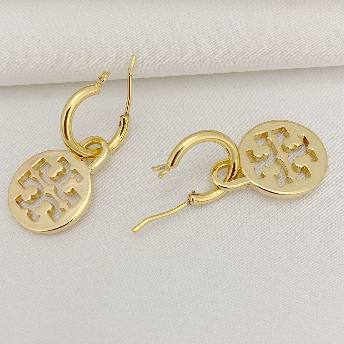Gold hoop earrings with circular disc charms on a light gray background