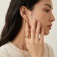 Woman wearing gold earrings and ring, with a neutral background