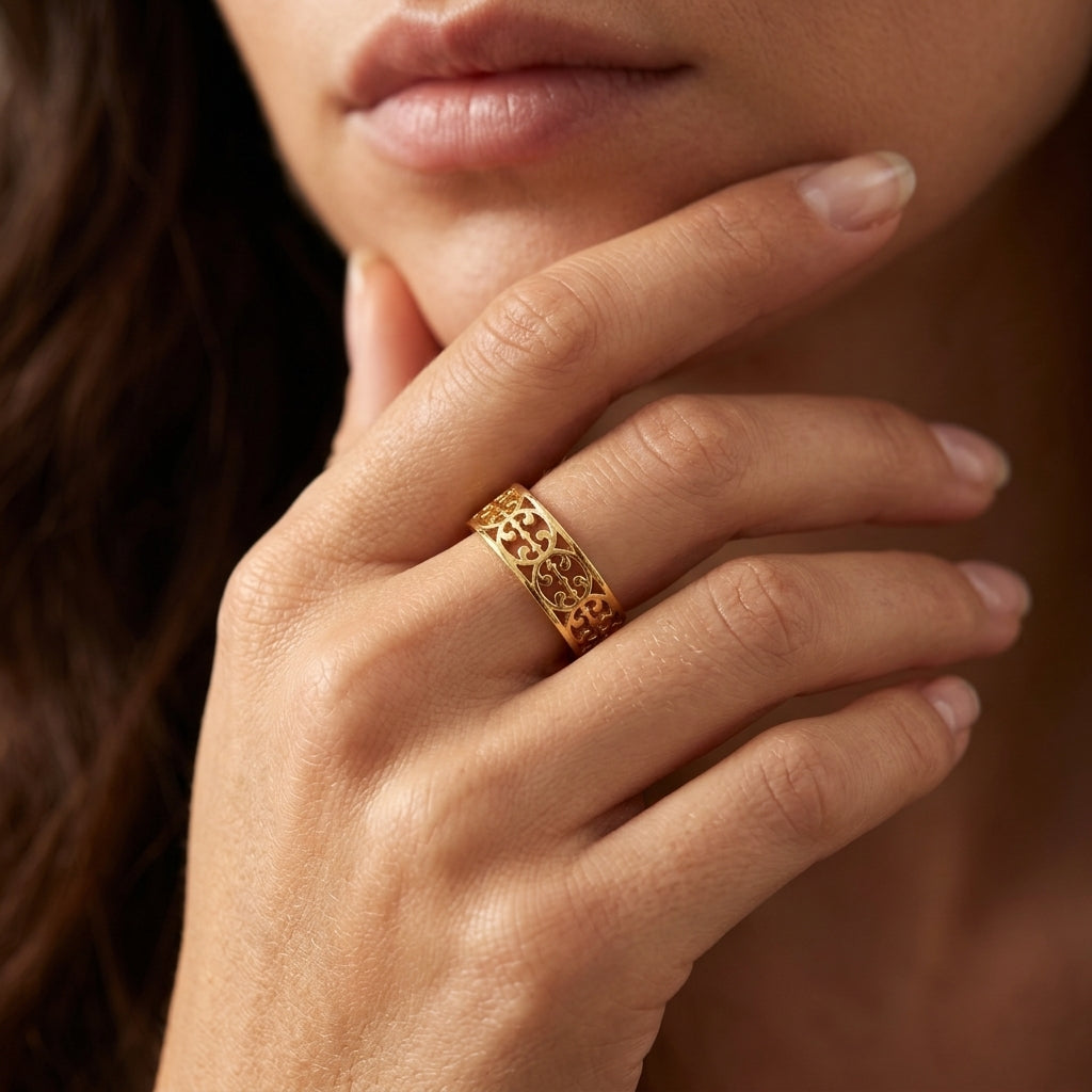A close-up of a woman's hand resting near her chin, wearing a wide gold ring with an intricate openwork filigree pattern.