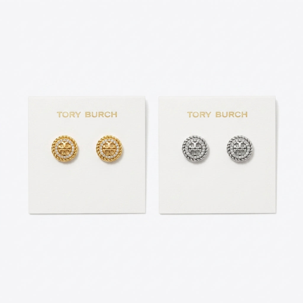 Two pairs of Tory Burch stud earrings displayed on white brand cards against a light gray background. The left card holds gold-tone circular studs with a raised star motif, and the right card holds silver-tone circular studs with the same star design.