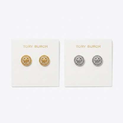 Two pairs of Tory Burch stud earrings displayed on white brand cards against a light gray background. The left card holds gold-tone circular studs with a raised star motif, and the right card holds silver-tone circular studs with the same star design.