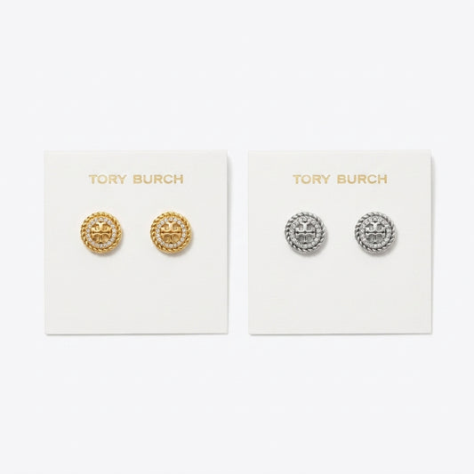 Two pairs of Tory Burch stud earrings displayed on white brand cards against a light gray background. The left card holds gold-tone circular studs with a raised star motif, and the right card holds silver-tone circular studs with the same star design.