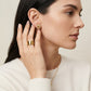 A close-up lifestyle shot of a woman wearing a gold ring and matching gold stud earring. The earring features a textured, floral-like gold pattern, while the ring is a wide, polished gold band.