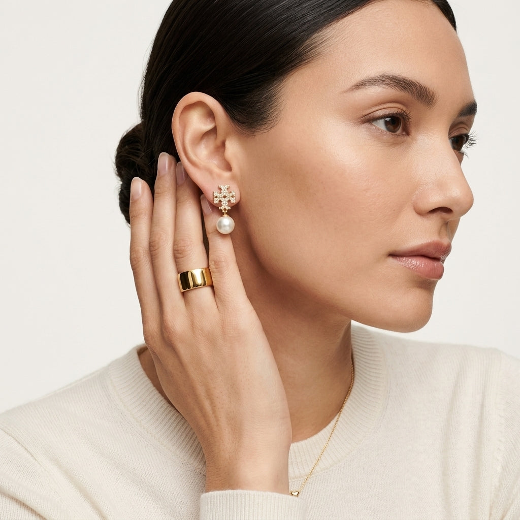 Woman wearing gold earrings and a ring, with a neutral background