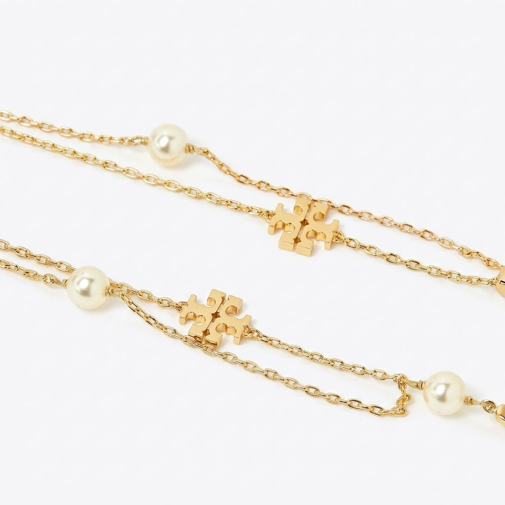 A gold chain necklace featuring small gold puzzle-piece charms and white pearl beads, displayed on a clean white background.
