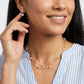 A close-up lifestyle shot of a woman wearing a gold double-layered necklace with small white pearls and gold floral charms, along with a matching gold stud earring.