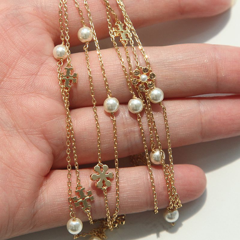 A close-up of a hand displaying multiple delicate gold chain necklaces adorned with small pearls and floral cross charms.