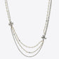 A multi-strand necklace featuring white faux pearls, silver-tone chains, and two small silver-tone cross pendants, displayed against a light gray background.