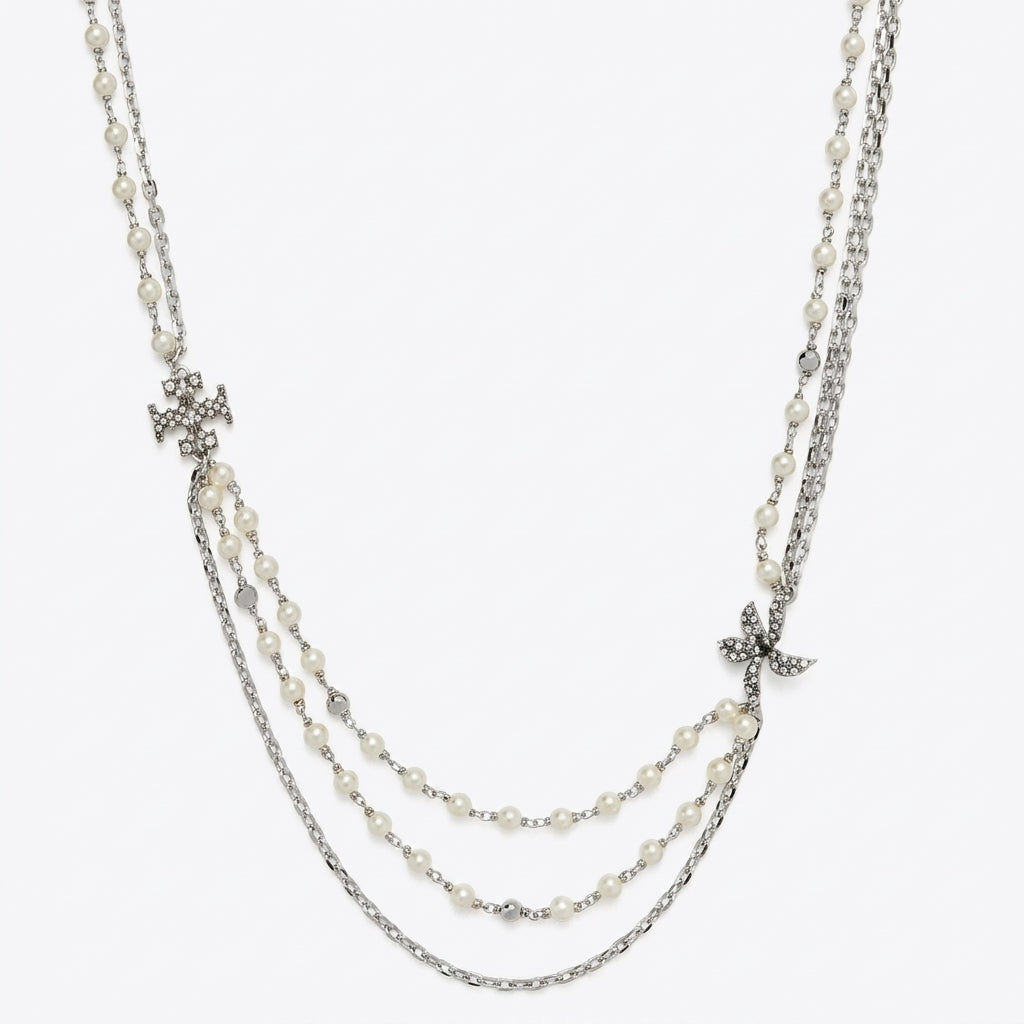 A multi-strand necklace featuring white faux pearls, silver-tone chains, and two small silver-tone cross pendants, displayed against a light gray background.