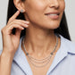 A close-up of a woman wearing a layered necklace set with white pearls and silver-toned starburst charms, styled with a light blue and white striped shirt.