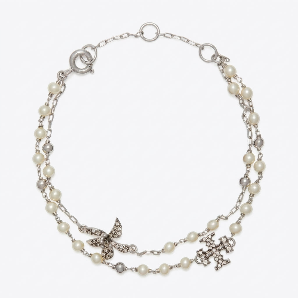 A silver-tone double-strand necklace featuring white faux pearls, a silver butterfly embellished with clear rhinestones, and a silver cross pendant, displayed on a light gray background.