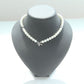 A pearl necklace with a silver dragonfly charm and clear rhinestone accents, displayed on a matte black jewelry bust against a white background.