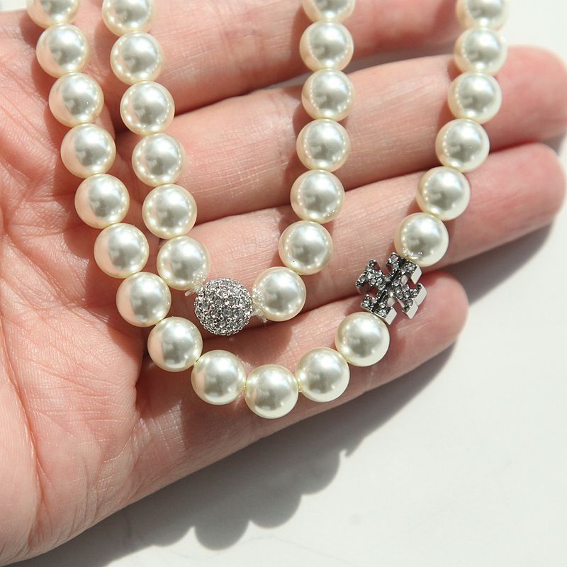 A close-up of a hand holding a double-strand pearl necklace with a silver-toned round pavé bead and a floral cluster charm.