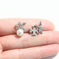 A pair of silver-toned butterfly stud earrings with clear rhinestones and a white pearl, shown resting on a person's fingers against a white background.