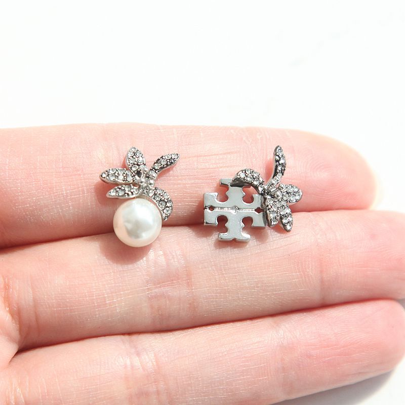 A pair of silver-toned butterfly stud earrings with clear rhinestones and a white pearl, shown resting on a person's fingers against a white background.
