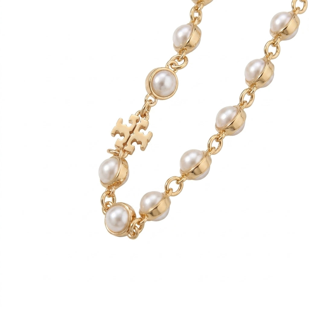 A gold chain necklace featuring irregular white freshwater pearls and a small gold monogram charm, shown on a plain white background.