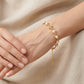 A delicate gold chain bracelet with white pearl accents worn on a woman's wrist, set against a soft beige linen background.