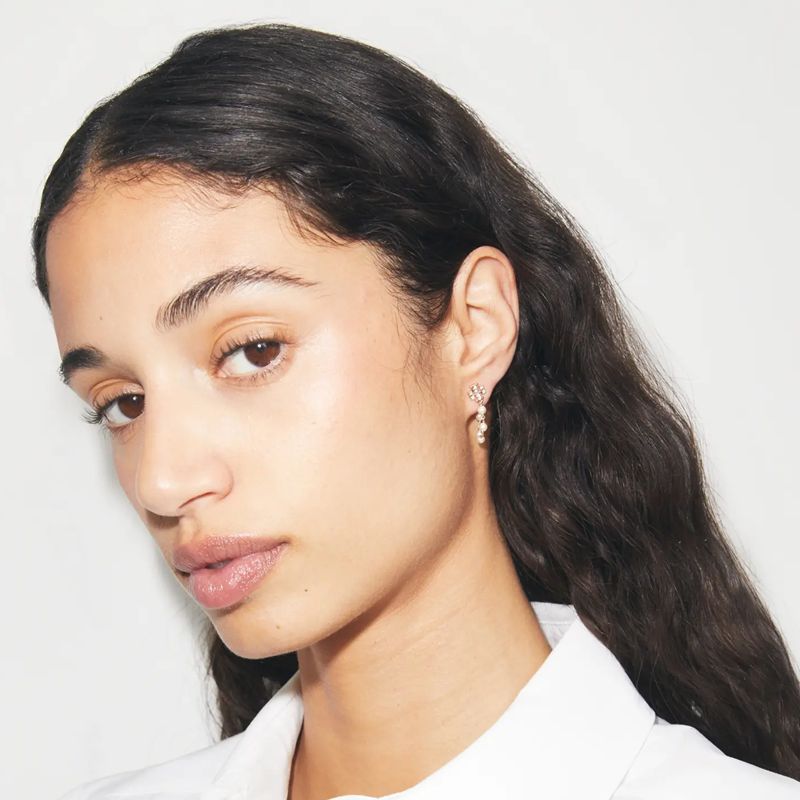 Woman with hair pulled back or tucked, the pearl and chain earrings catching light at the earlobe — luminous, feminine, graceful.