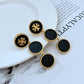 Black and gold earrings on a white plate with a newspaper background