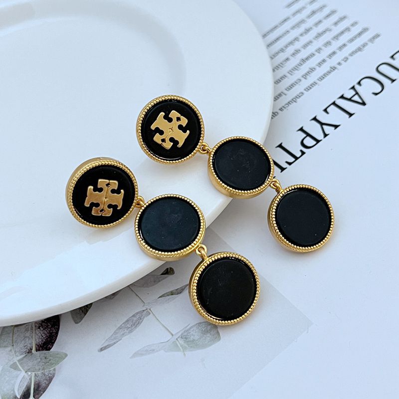Black and gold earrings on a white plate with a newspaper background