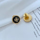 Gold and black earring on a white surface with text