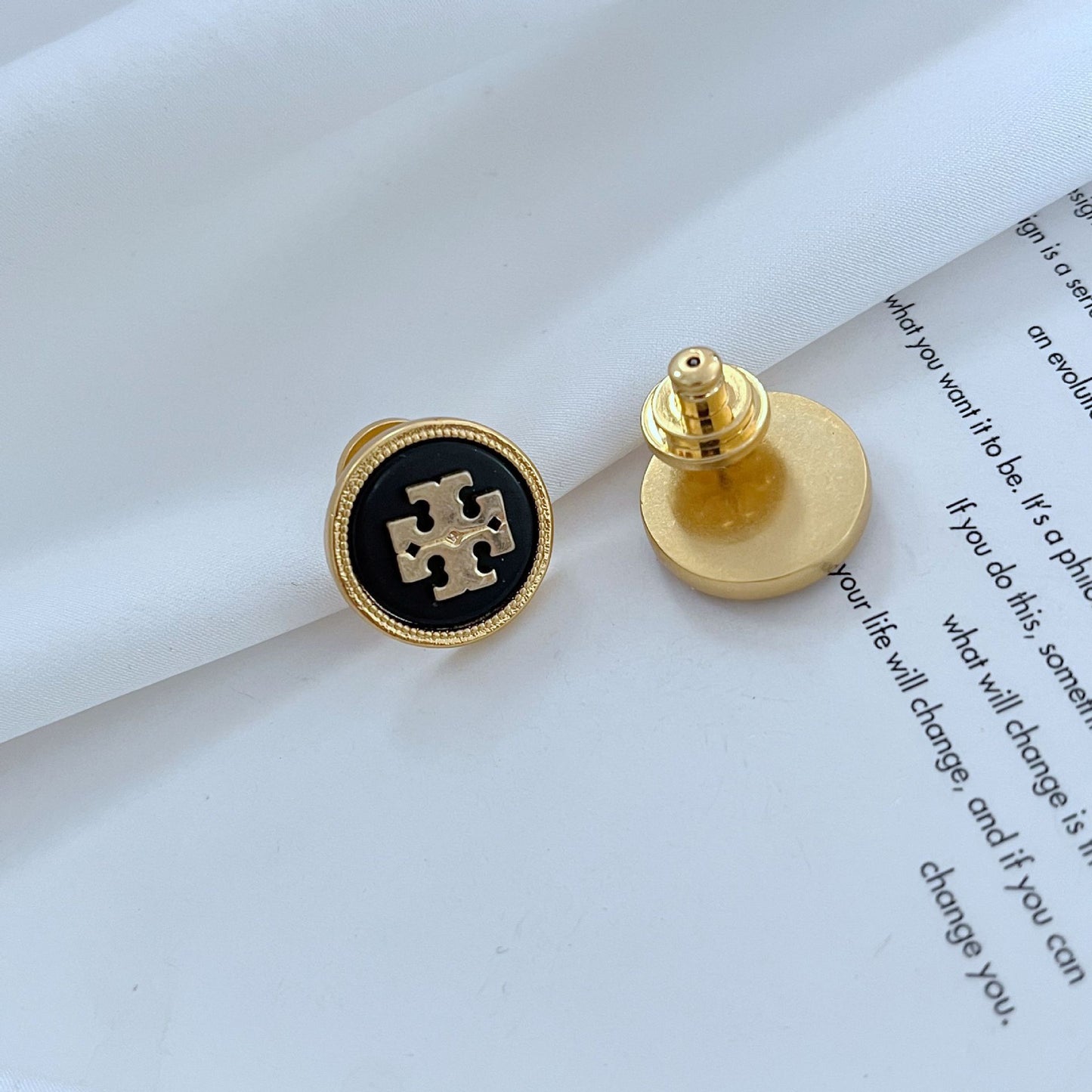 Gold and black earring on a white surface with text