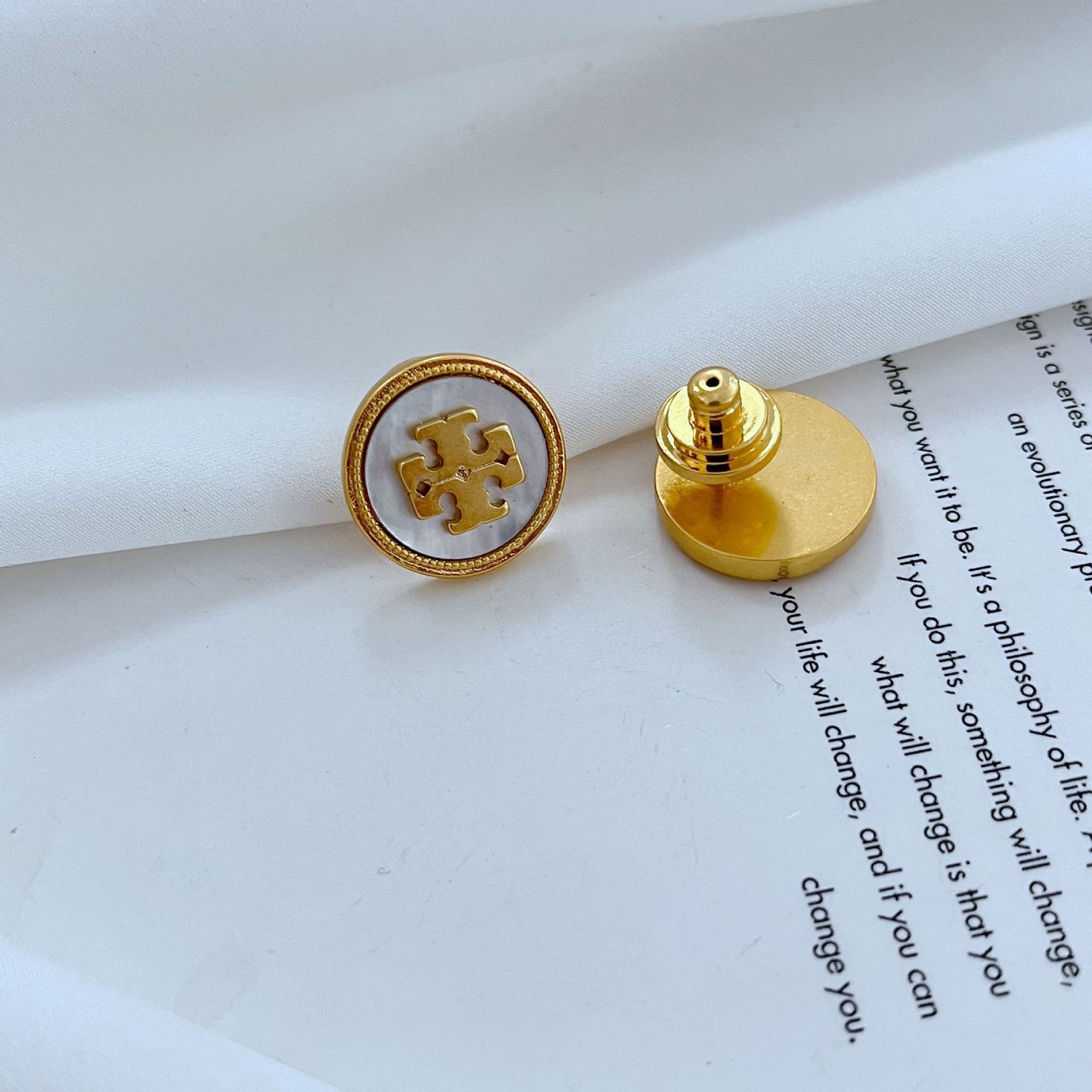 Gold earring with a logo on a white surface