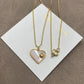 The necklace and earrings displayed together on a soft, light background (gray velvet or linen), showcasing the matching heart designs and iridescent pearl finish