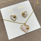 The necklace and earrings displayed together on a soft, light background (gray velvet or linen), showcasing the matching heart designs and iridescent pearl finish