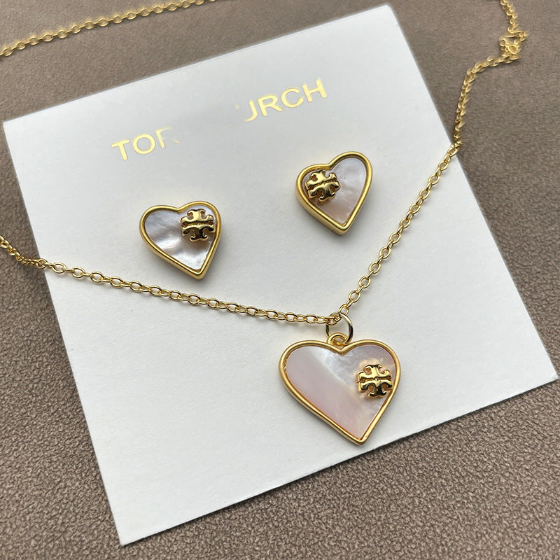 The necklace and earrings displayed together on a soft, light background (gray velvet or linen), showcasing the matching heart designs and iridescent pearl finish