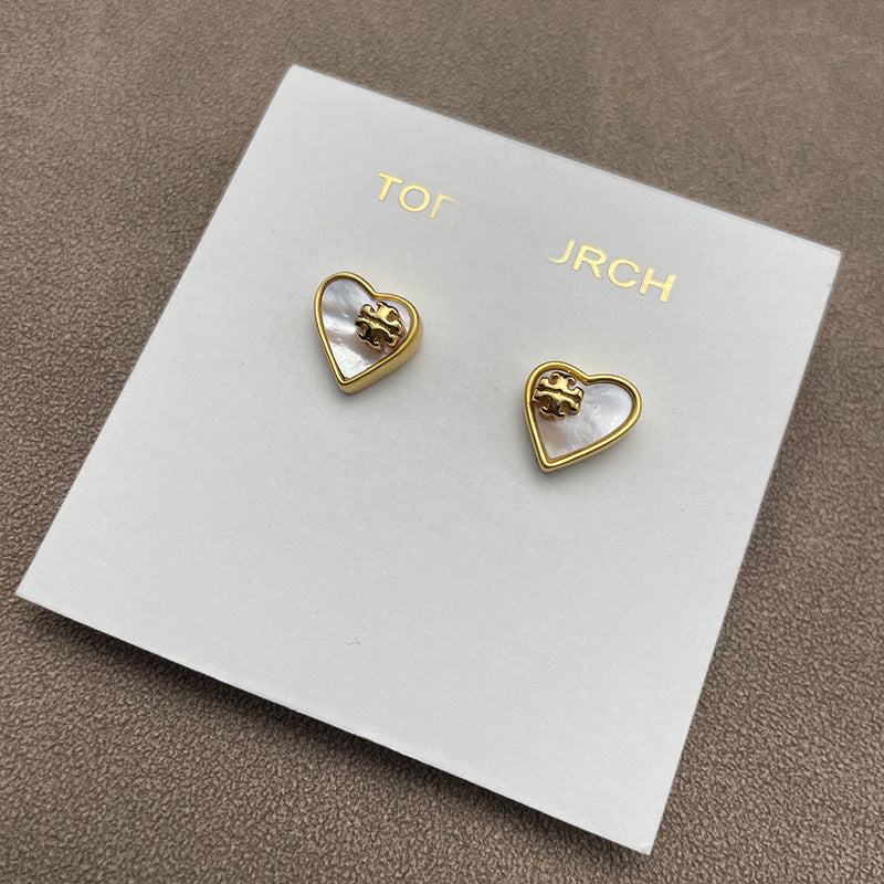 The necklace and earrings displayed together on a soft, light background (gray velvet or linen), showcasing the matching heart designs and iridescent pearl finish