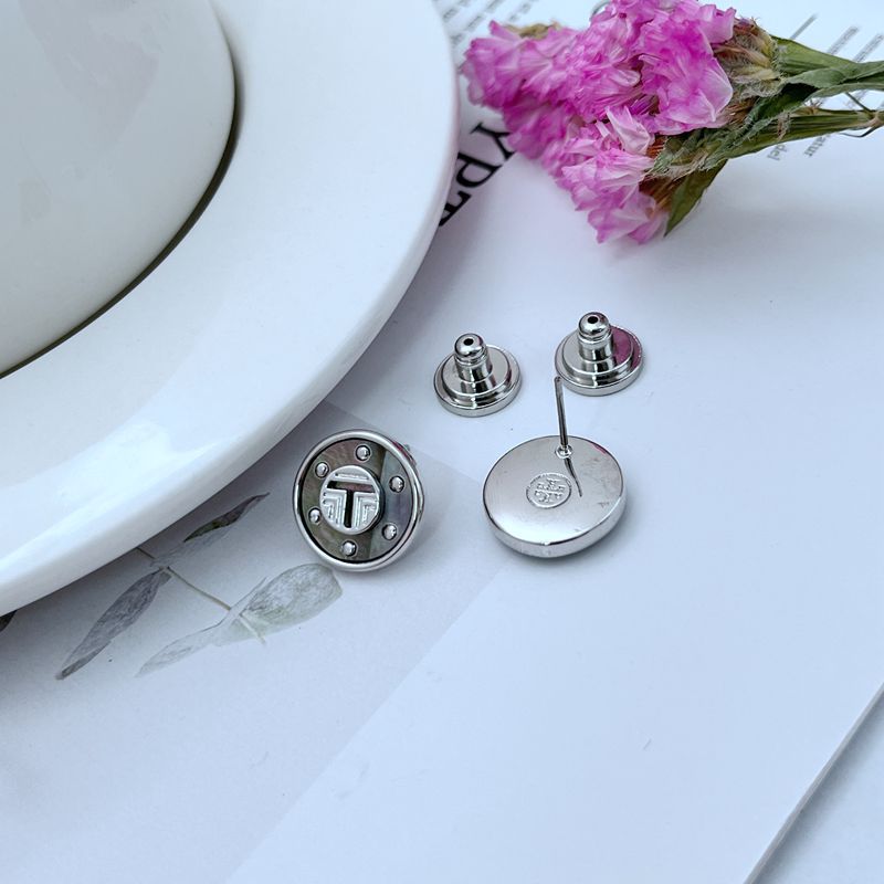 The studs placed on a seashell, a bed of sand, or next to other natural elements like a sprig of eucalyptus, reinforcing the organic, coastal-inspired aesthetic.