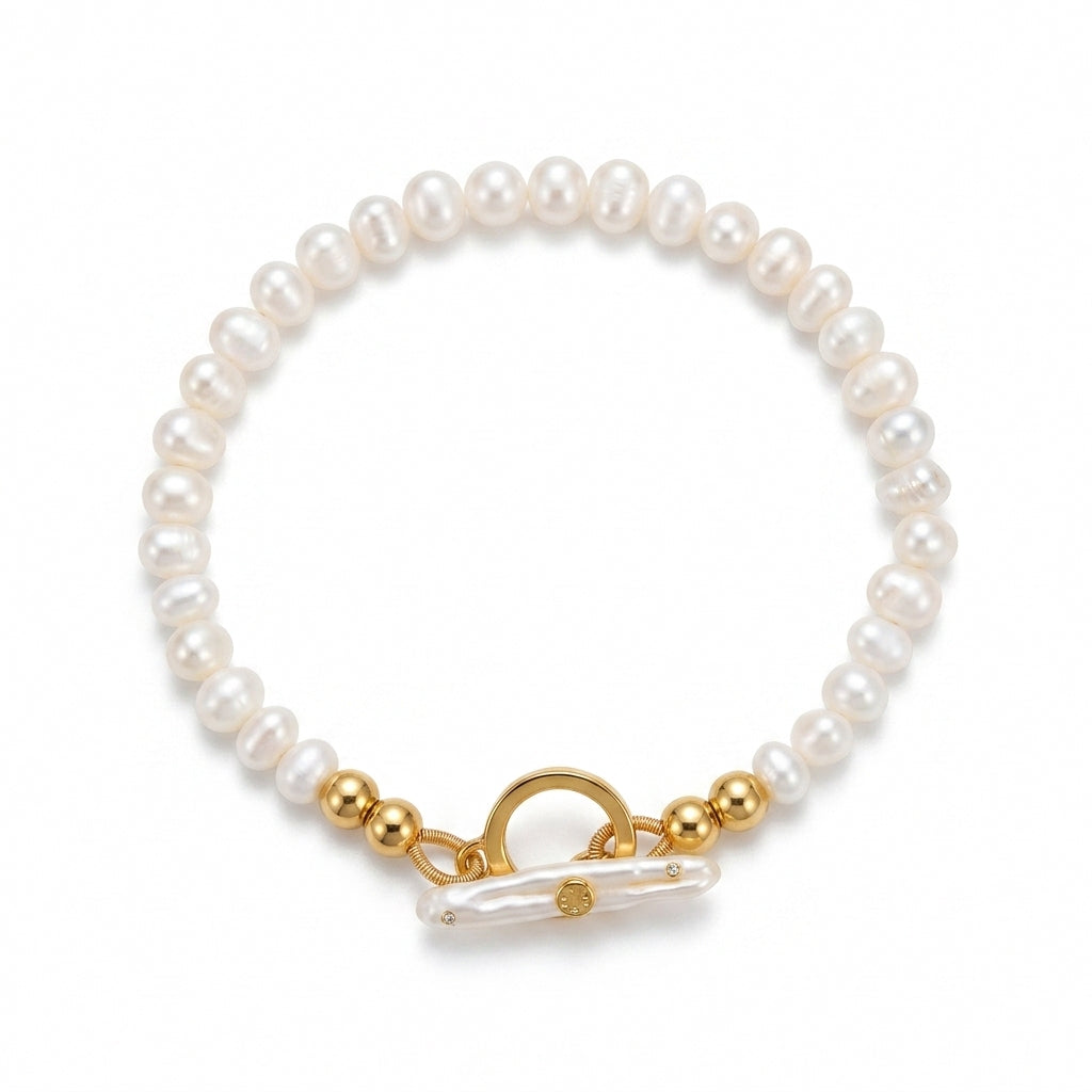 A beaded bracelet featuring white freshwater pearls, polished gold spacer beads, and a gold toggle clasp with a clear resin accent, shown on a plain white background.