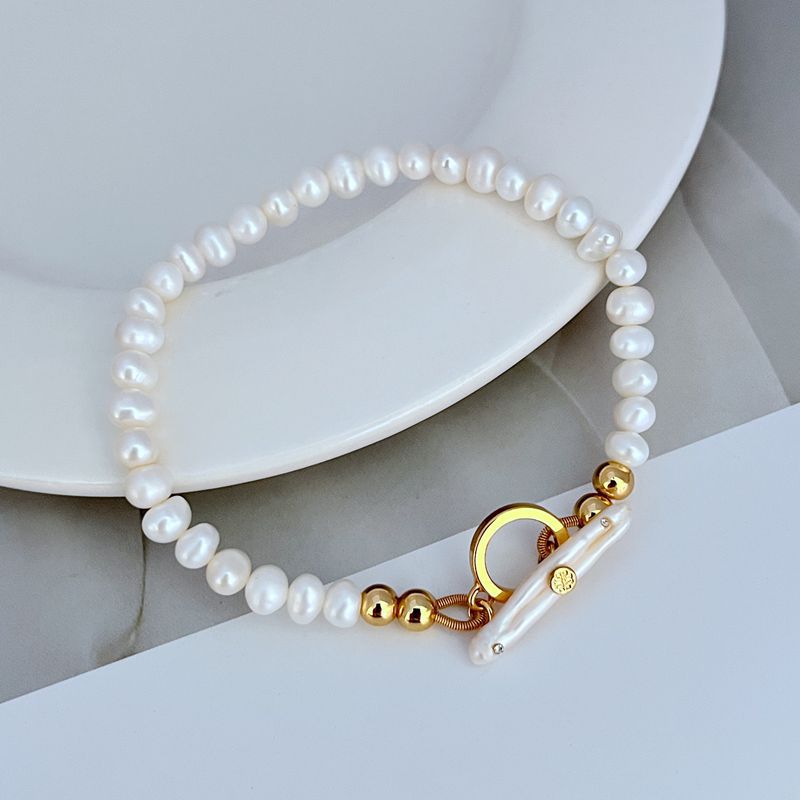Bracelet laid flat on a textured sandy-beige or sea-inspired background, highlighting the organic shapes of pearls and shell pieces.