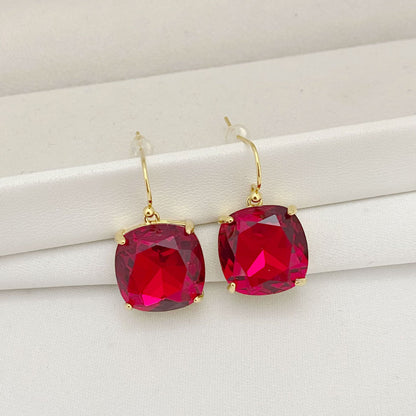 Gold earrings with red gemstones on a white surface