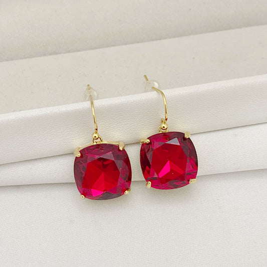 Gold earrings with red gemstones on a white surface