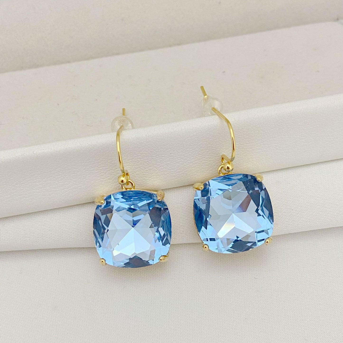 Gold earrings with blue gemstones on a beige background