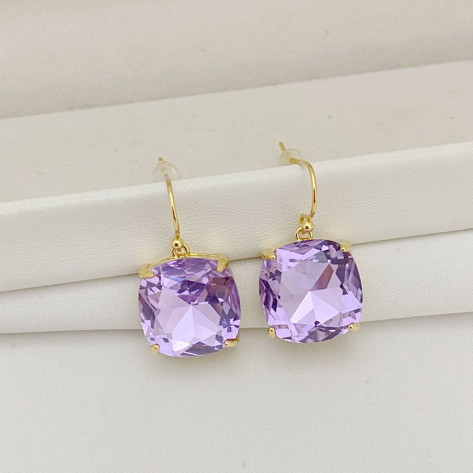 Purple gemstone earrings with gold hooks on a white surface