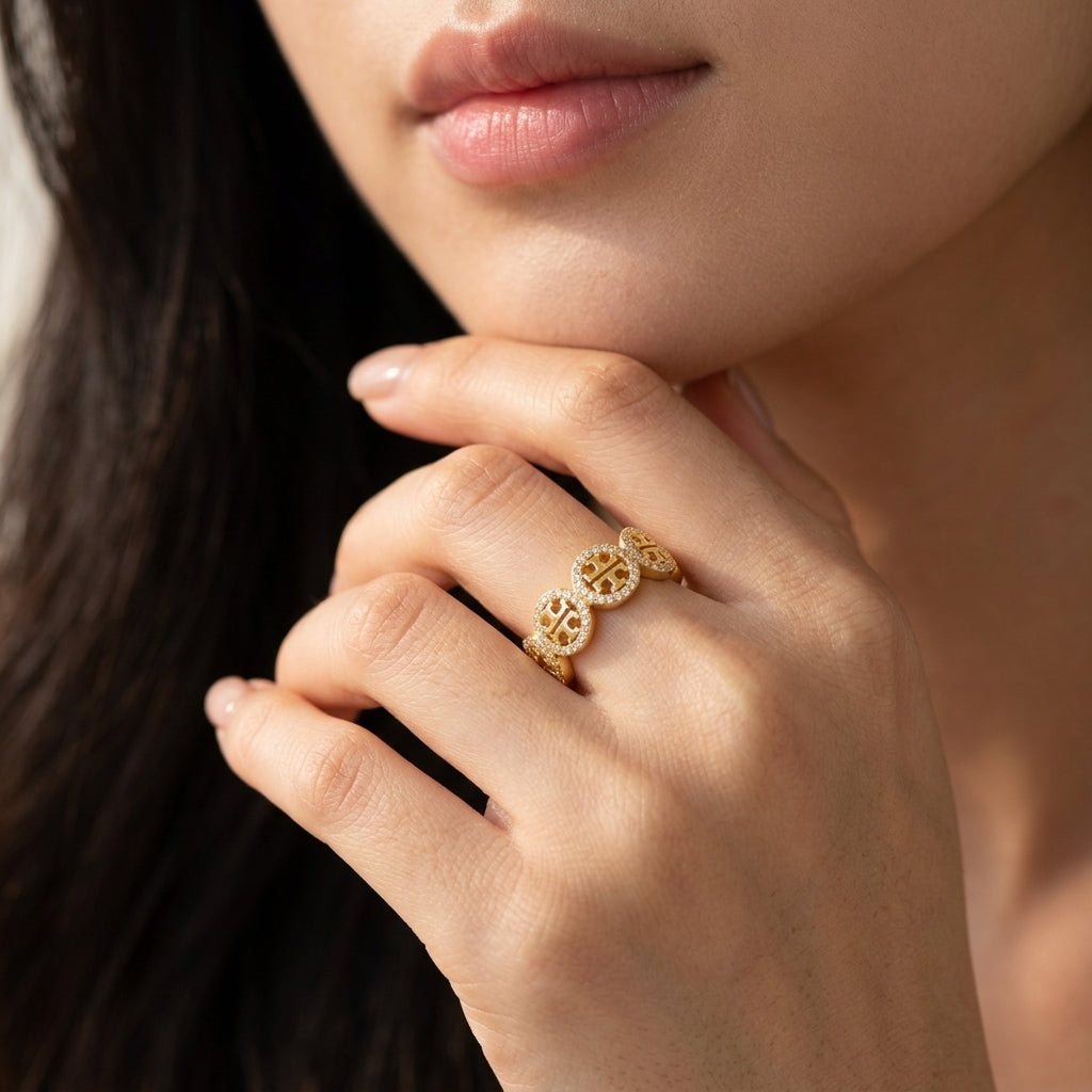 A close-up lifestyle shot of a model's hand wearing a delicate gold ring with three interlocking circular medallion motifs.