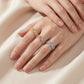 Three delicate filigree rings in yellow gold, rose gold, and silver, worn on a woman's hand against a soft beige satin background.