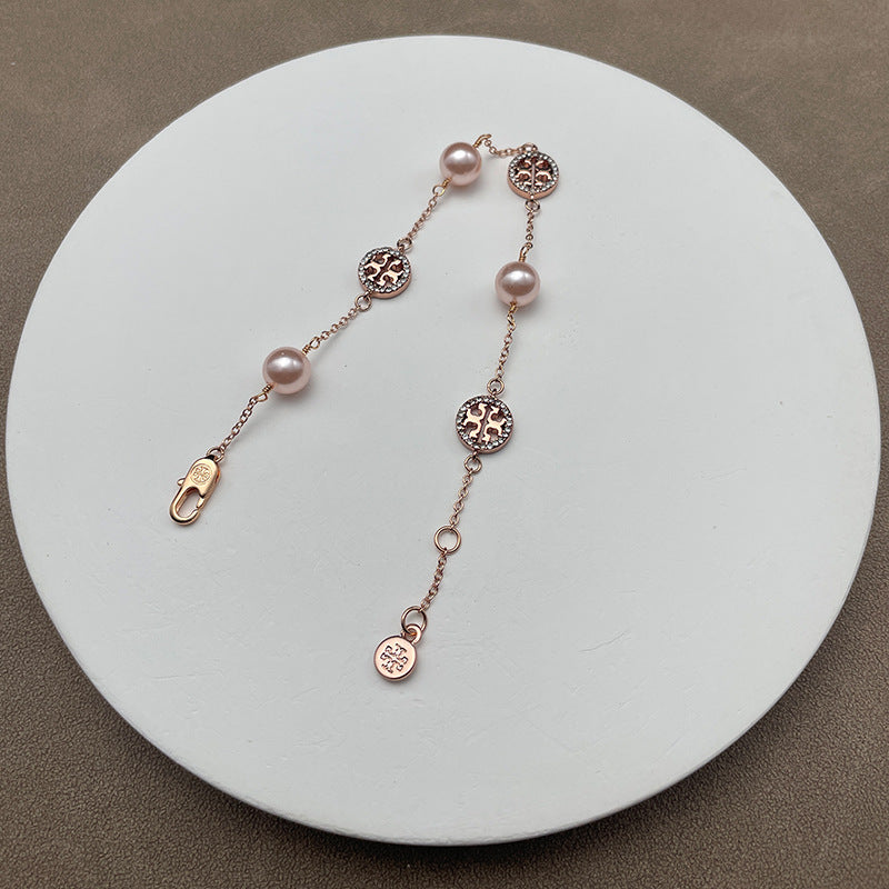 Bracelet laid flat on a soft, neutral background (light gray suede or linen), highlighting the pearl luster and gold chain detailing.