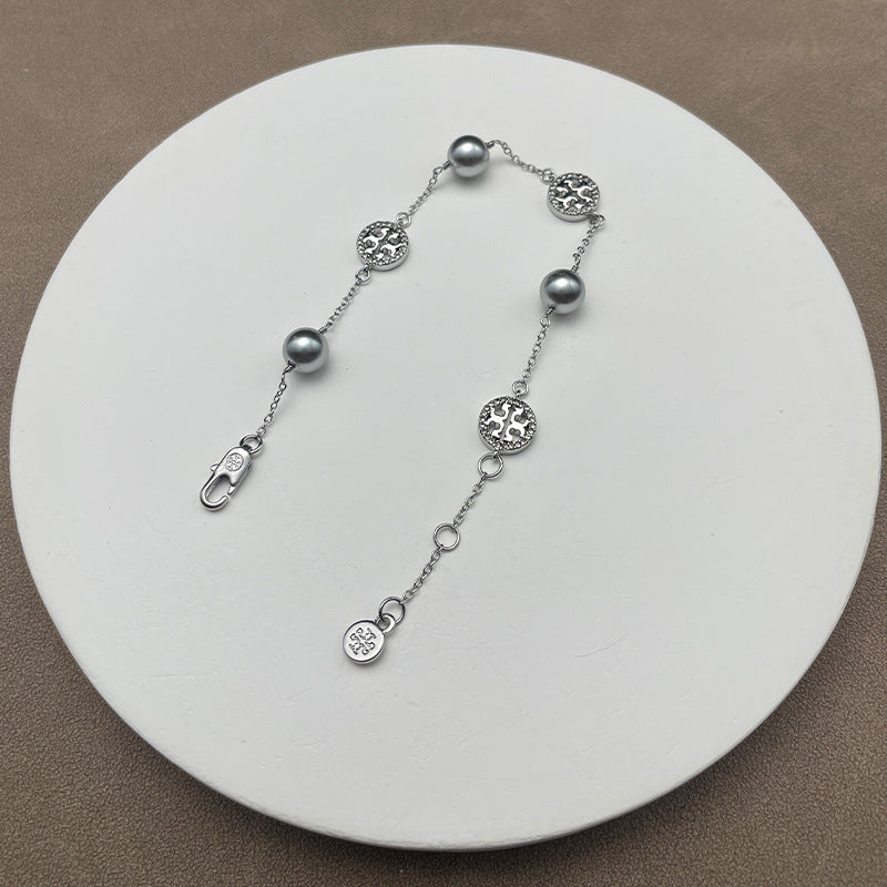 Bracelet laid flat on a soft, neutral background (light gray suede or linen), highlighting the pearl luster and gold chain detailing.