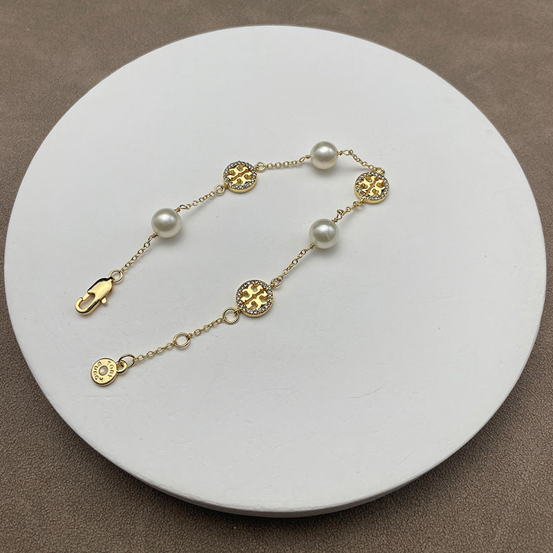 Bracelet laid flat on a soft, neutral background (light gray suede or linen), highlighting the pearl luster and gold chain detailing.