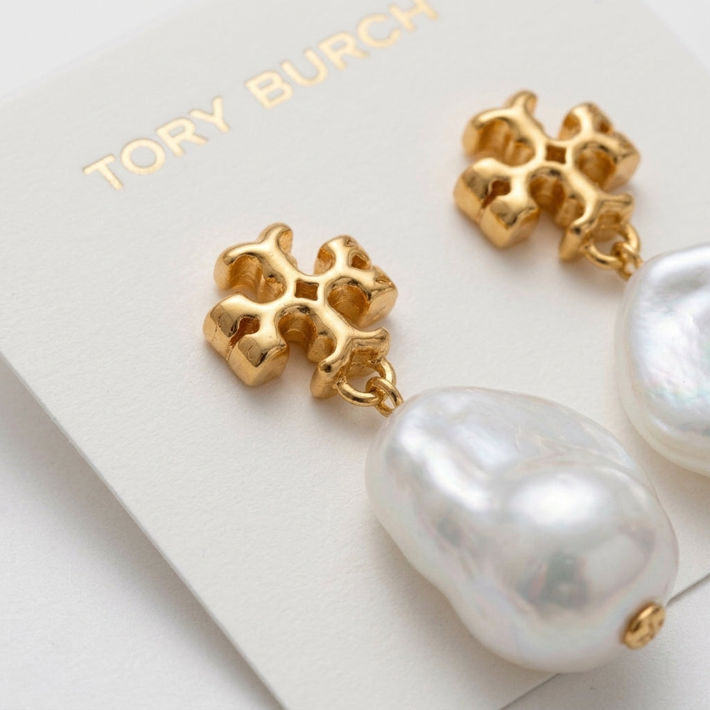 Tory Burch gold-tone earrings with a textured four-petal flower design and a large baroque pearl drop, displayed on a white branded card.