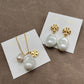 Both earrings displayed face-up on a soft, neutral background (light gray or ivory suede), highlighting the pearl’s luster and gold setting.
