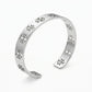 A silver open cuff bracelet featuring a repeating geometric cutout pattern, displayed on a clean white background.