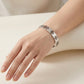A close-up of a person's hand and wrist wearing a polished silver cuff bracelet engraved with Chinese characters.
